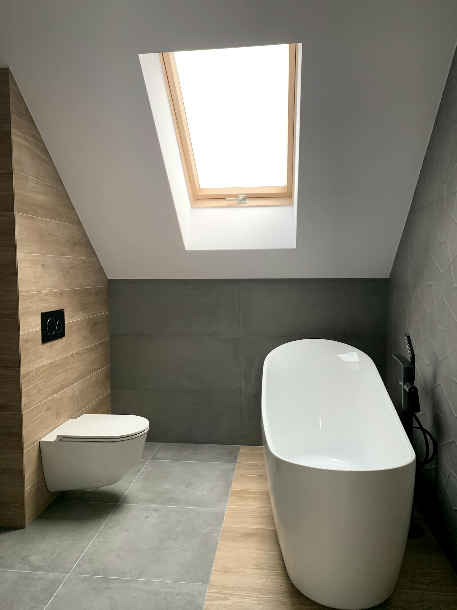 Modern interior of stylish minimal attic bathroom with white bathtub and toilet and roof window